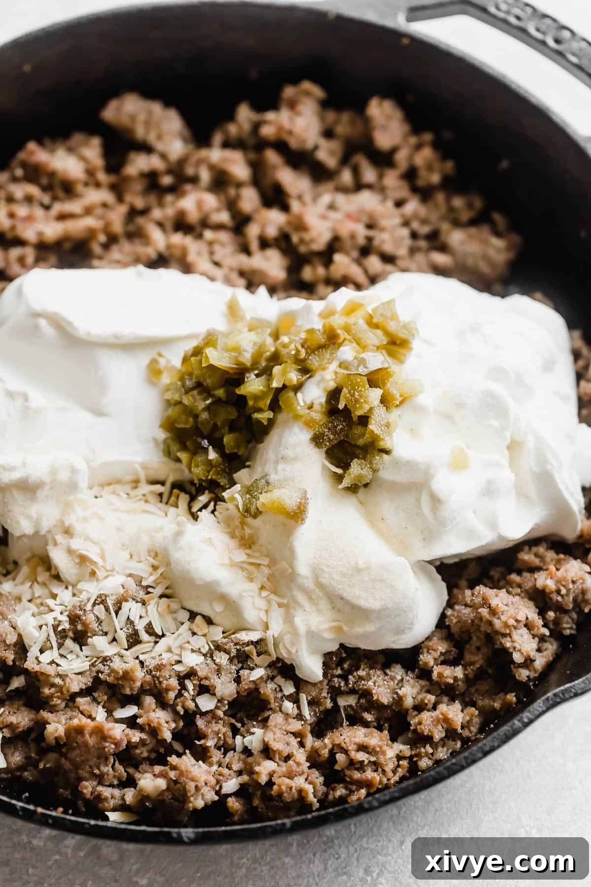 Jimmy dean sausage cookies in a skillet with cream cheese and chopped jalapeños overtop.