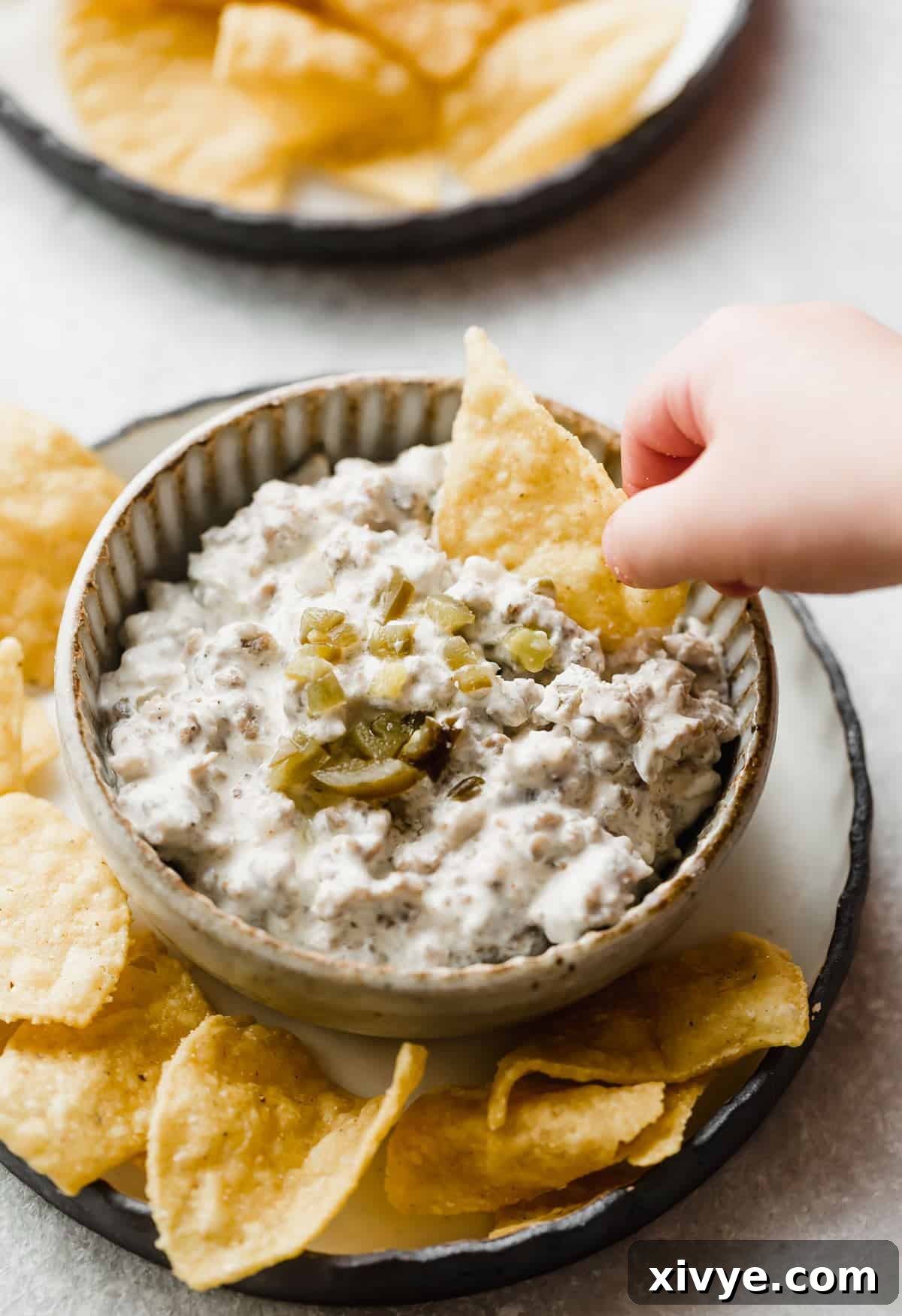 A hand dipping a tortilla chip into a bowl full of Cream Cheese Sausage Dip.