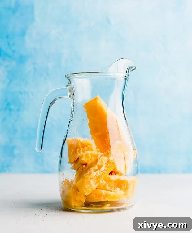 A clear glass pitcher containing chunks of frozen peach punch, ready to be mixed with soda.