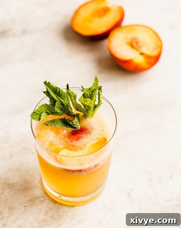 An inviting glass of orange-colored peach punch, with a blurred sliced peach in the background, hinting at fresh ingredients.