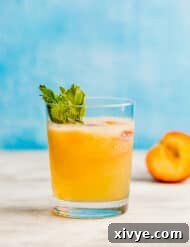 A glass full of peach punch in front of a blue background.