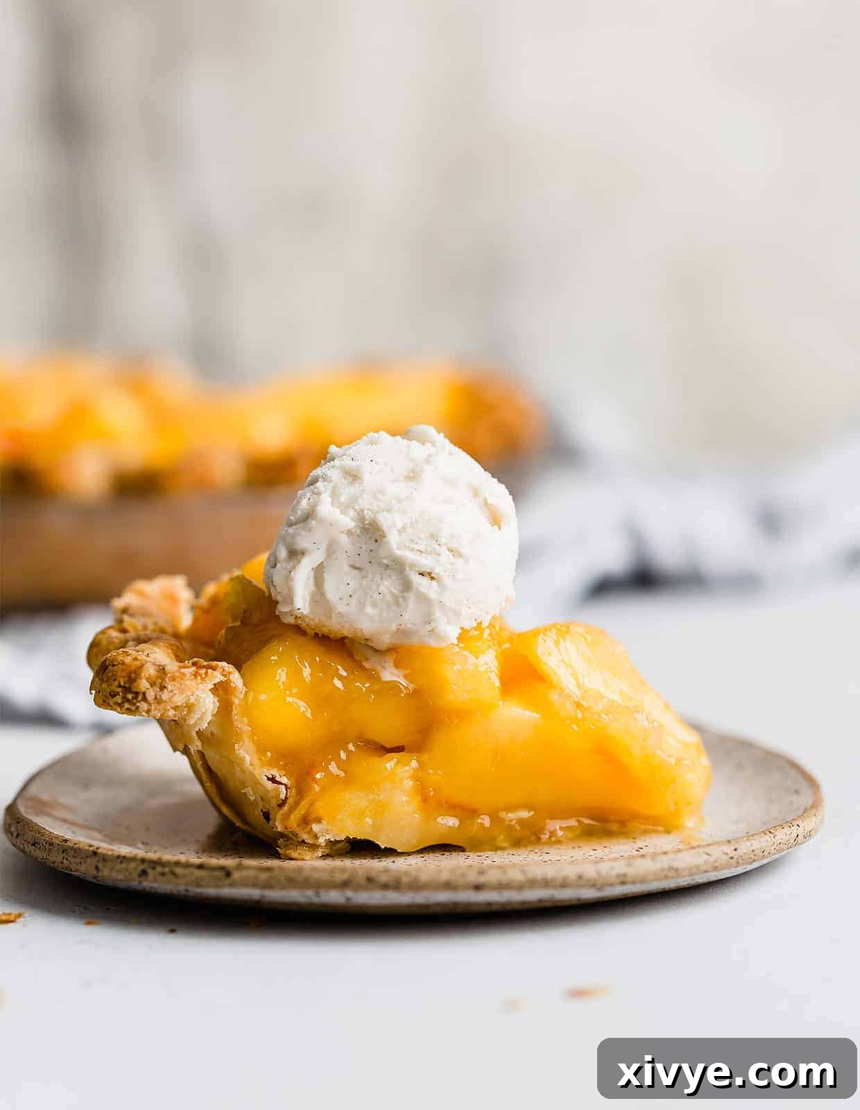A slice of peach pie topped with a scoop of vanilla ice cream, against a white background.