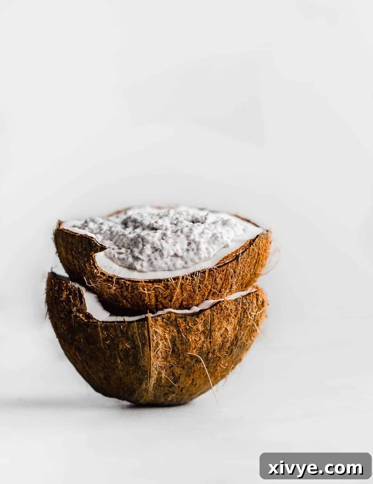 A raw coconut filled with Overnight Coconut Chia Pudding against a white background.
