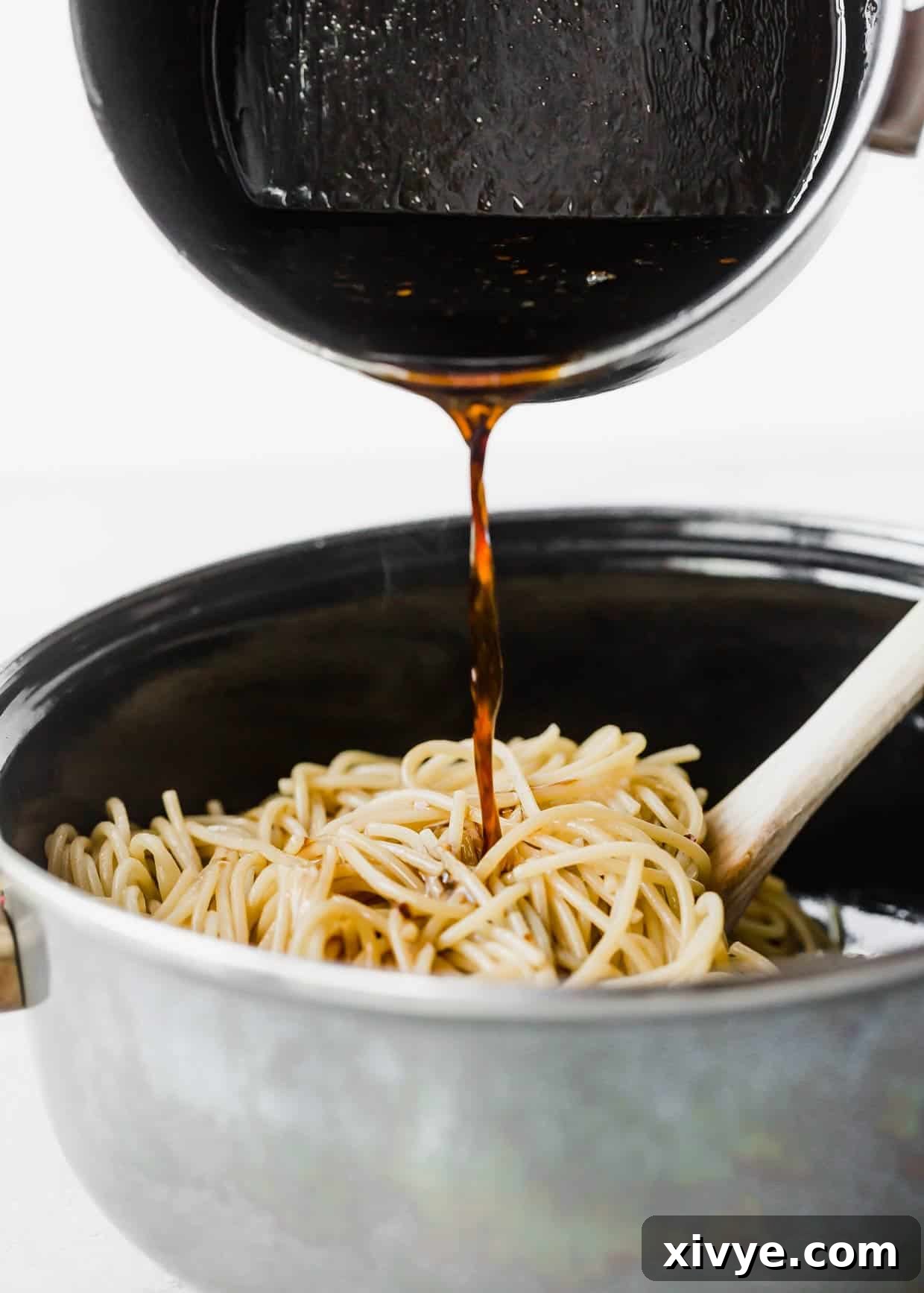 Savory Sesame Noodles 5 A sesame oil and soy sauce based sauce being poured overtop spaghetti noodles in a black pot.