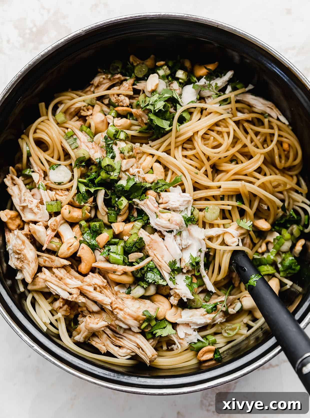 Savory Sesame Noodles 6 A black pot with spaghetti noodles coated in a sesame cilantro sauce topped with chicken, green onions, and cilantro.
