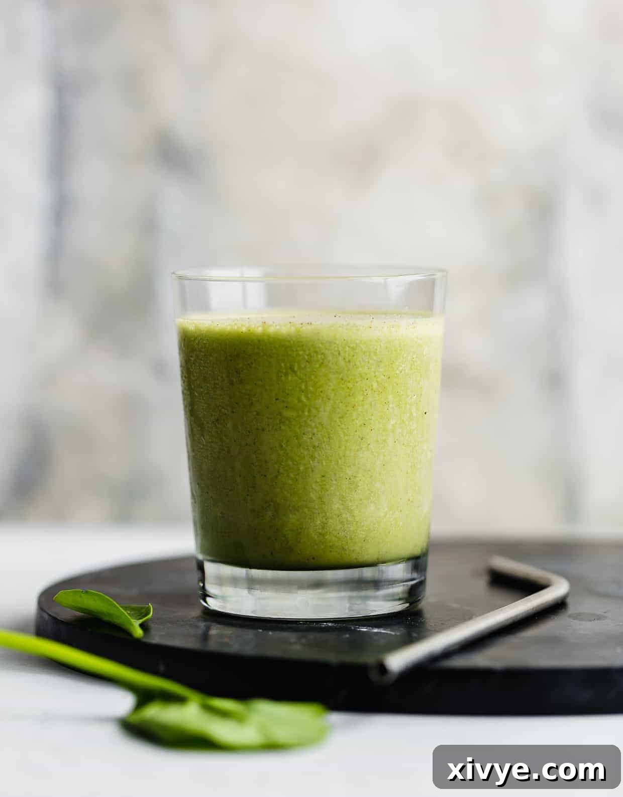 Energizing Banana Spinach Protein Smoothie 6 A green smoothie in a cup with spinach leaves in the foreground.