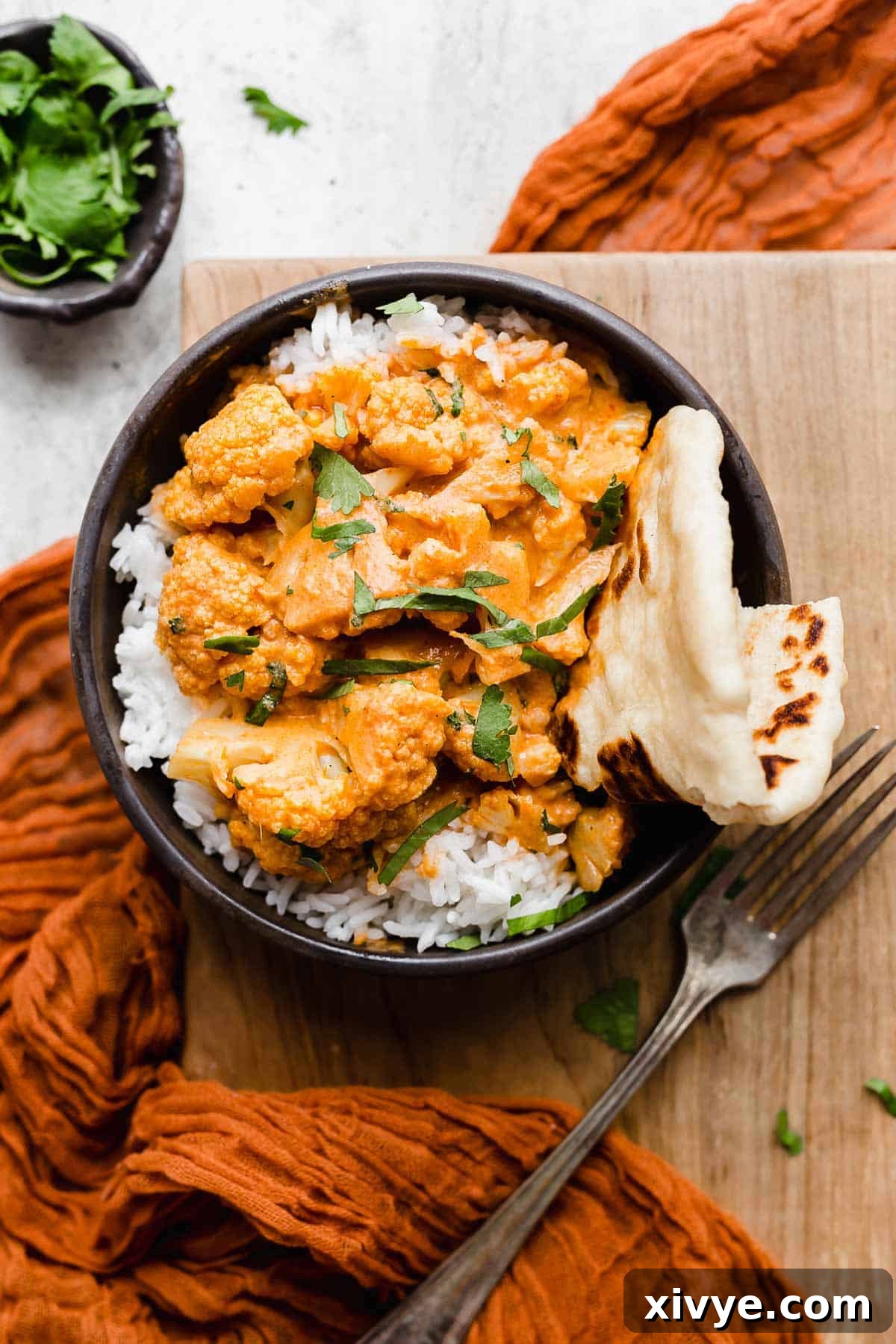 Overhead photo of Indian Butter Cauliflower overtop a bed of white rice in a black bowl and garnished with fresh cilantro.