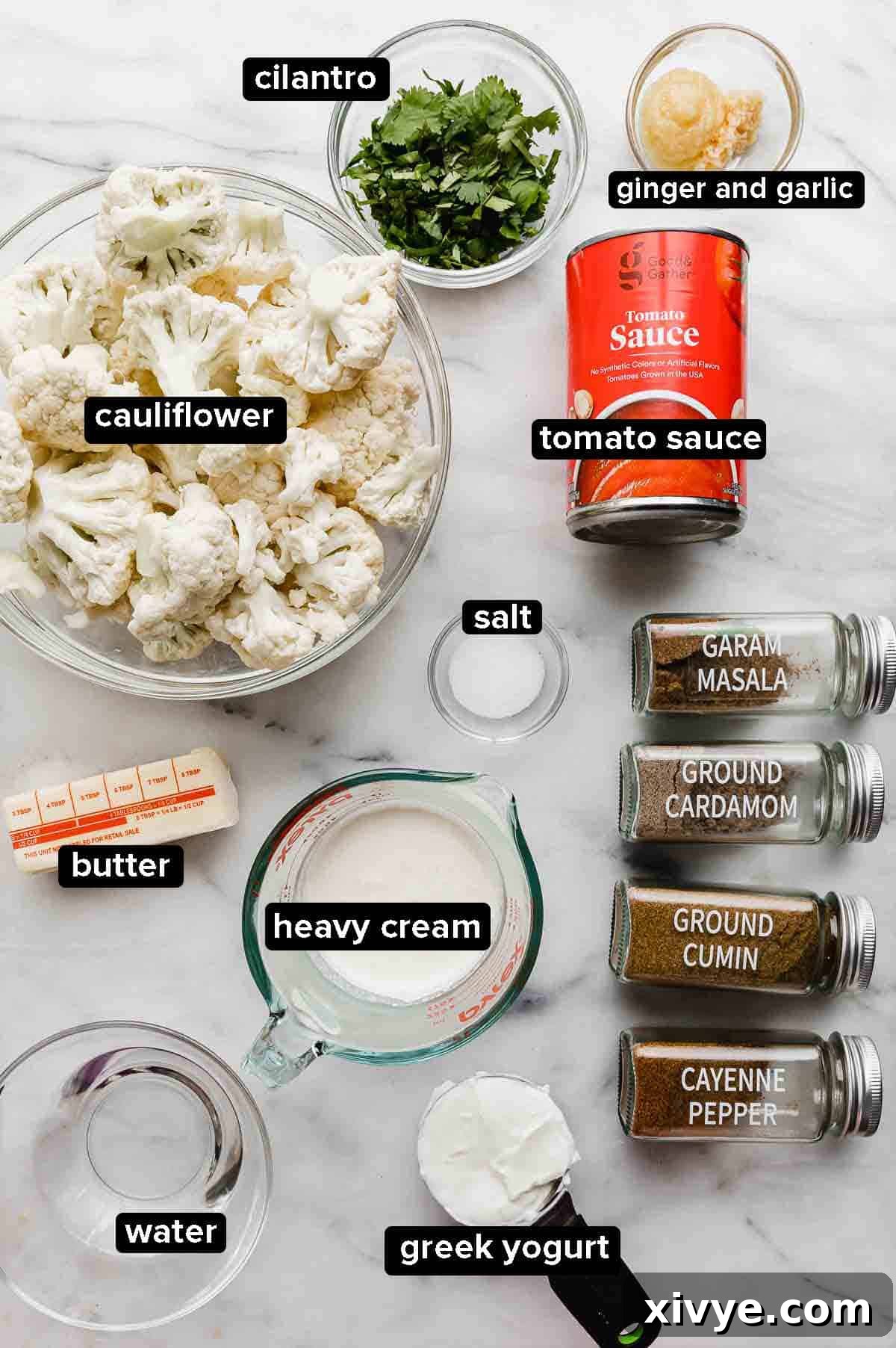 Indian Butter Cauliflower ingredients portioned into glass bowls on a white marble background.