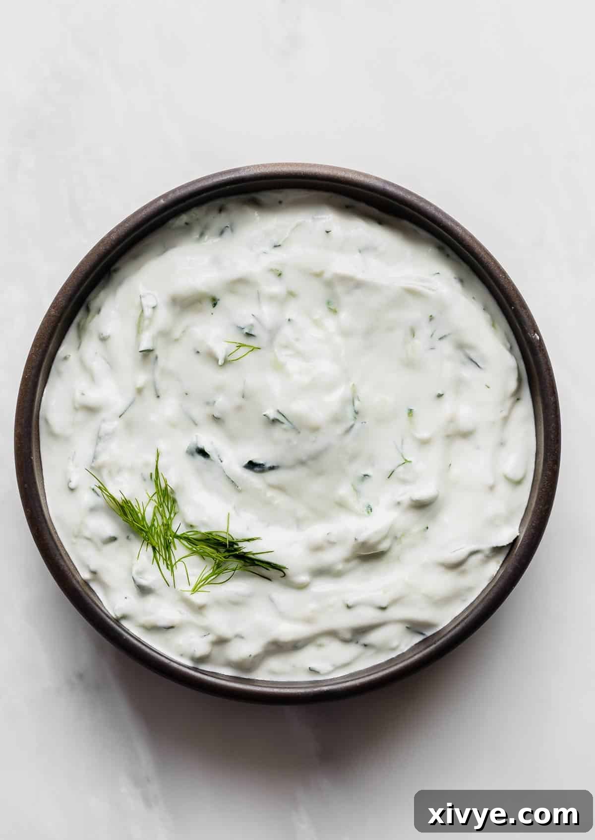 A black rimmed bowl filled with authentic Tzatziki sauce using shredded cucumber and fresh dill, on a white background, invitingly prepared for dipping.