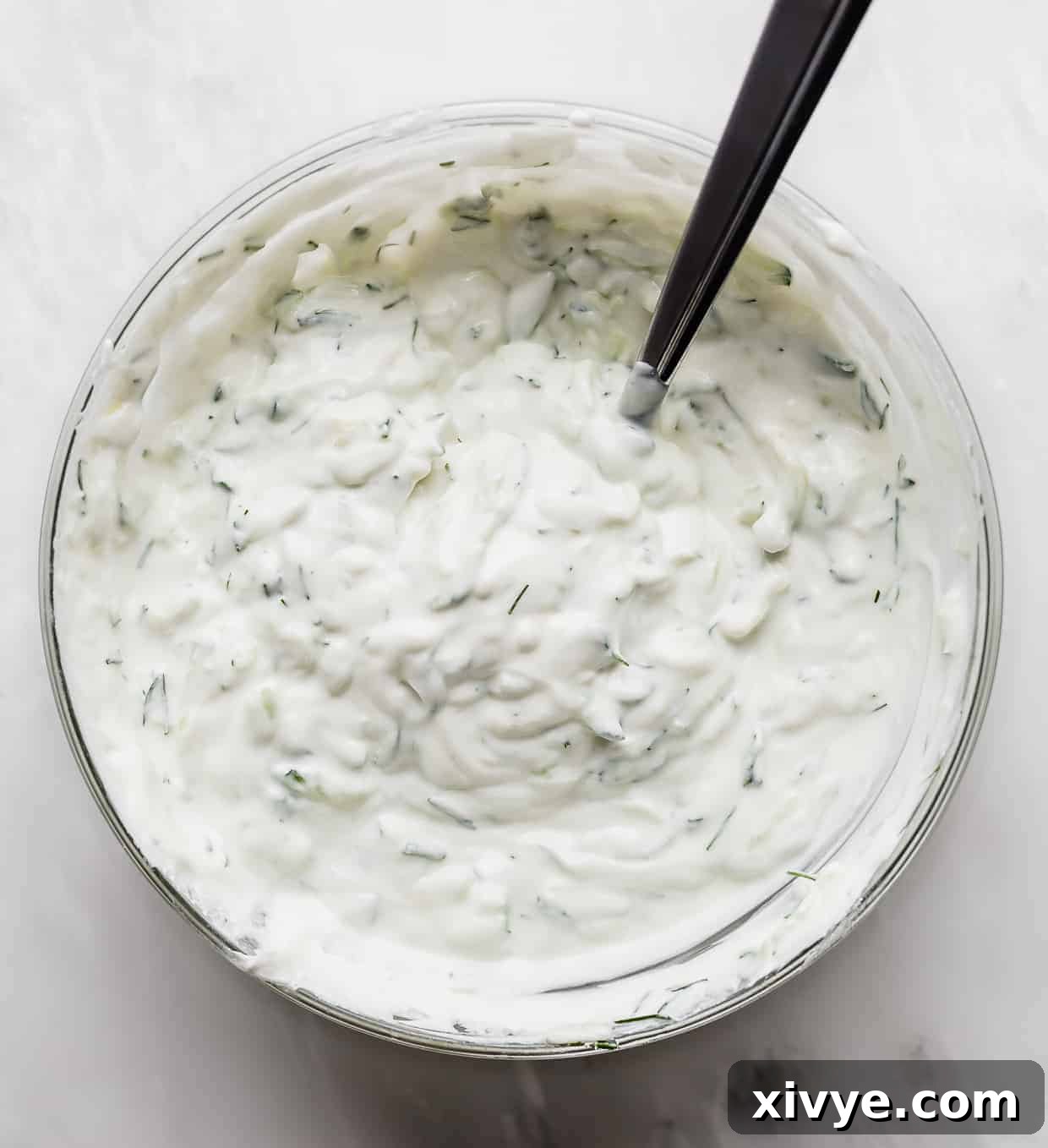 A simple yet elegant bowl of homemade Tzatziki sauce, showcasing its creamy texture and fresh dill, presented on a pristine white background.