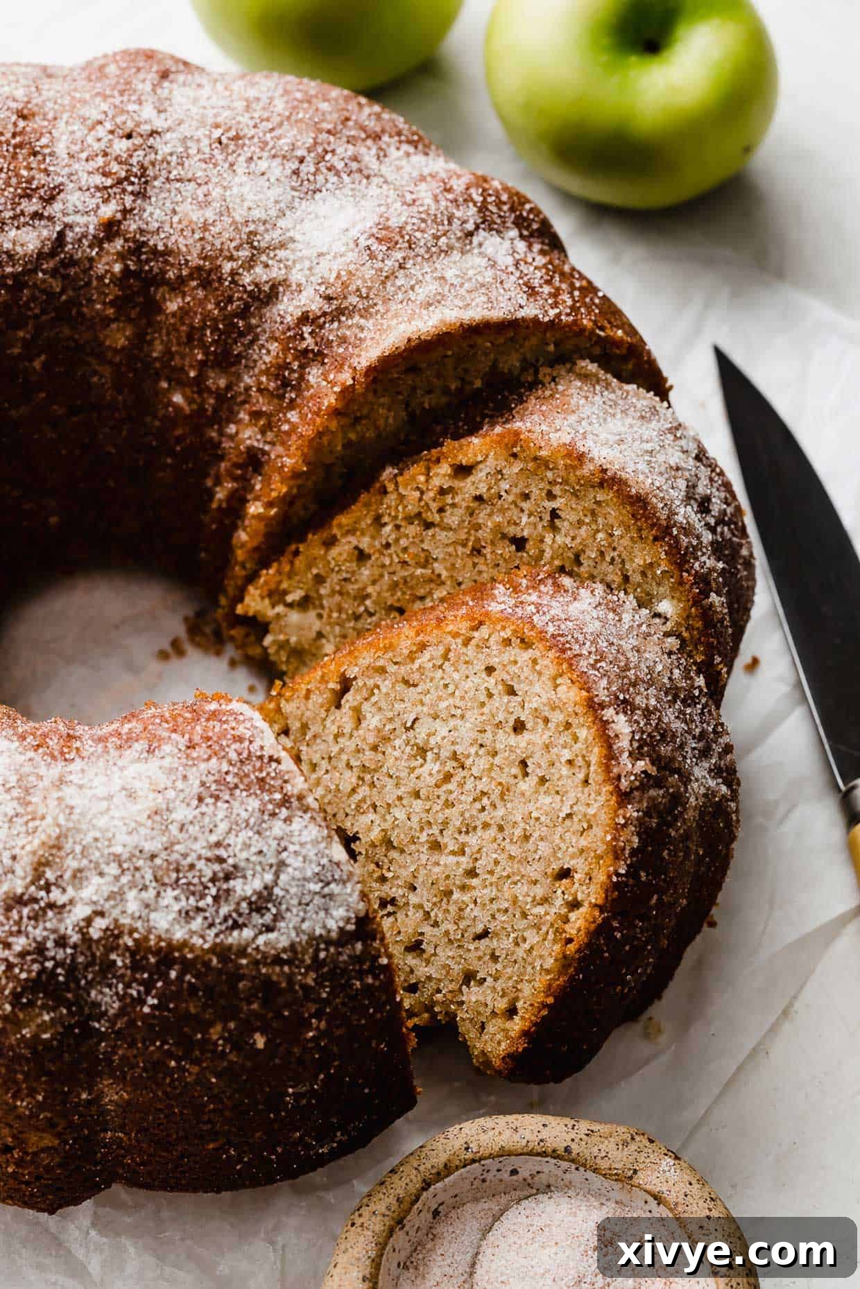 An Apple Cider Bundt Cake topped with sugar with green apples in the background.