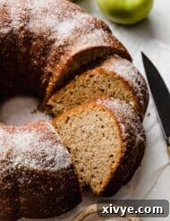 An Apple Cider Bundt Cake topped with sugar with green apples in the background.