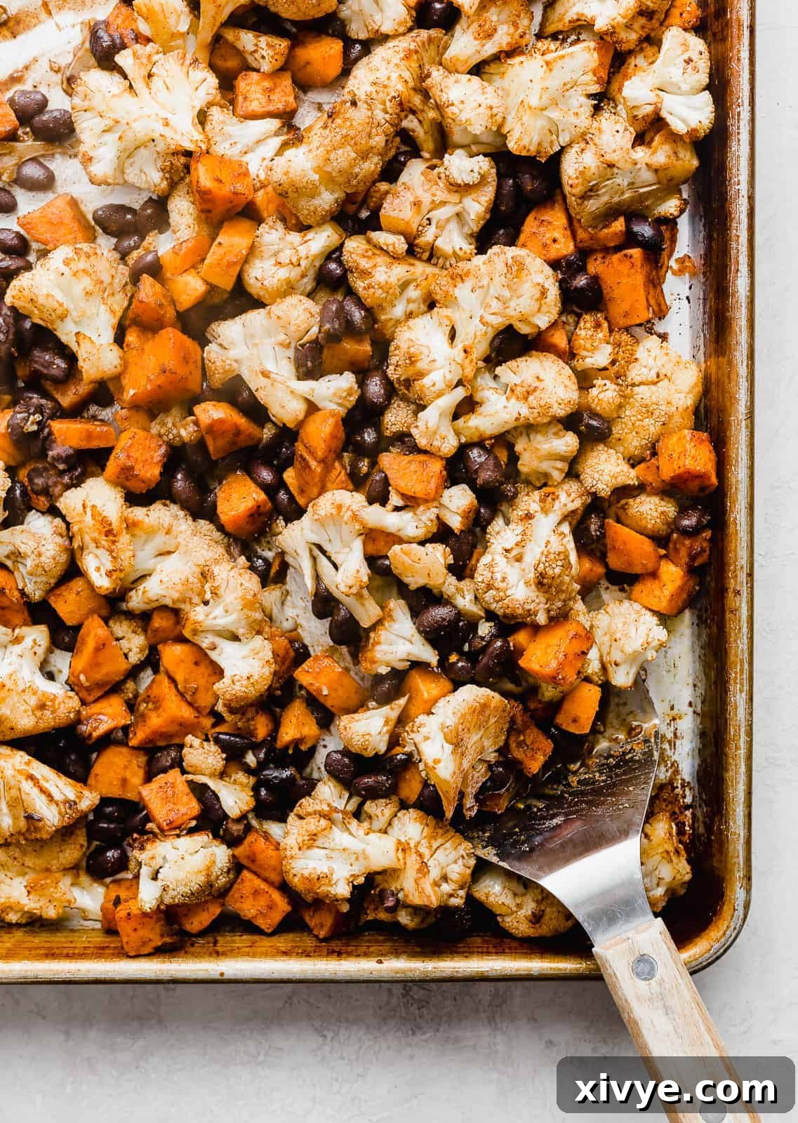 A baking sheet showcasing perfectly roasted sweet potatoes and cauliflower, now joined by warmed black beans, fresh out of the oven.