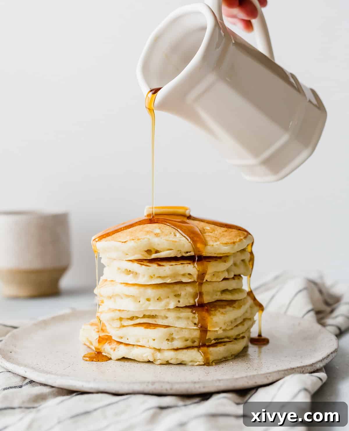 Grandma's Fluffy Buttermilk Pancakes 62 Golden maple syrup being generously poured over a towering stack of perfectly fluffy buttermilk pancakes, presented on a pristine white plate, promising a delightful breakfast.