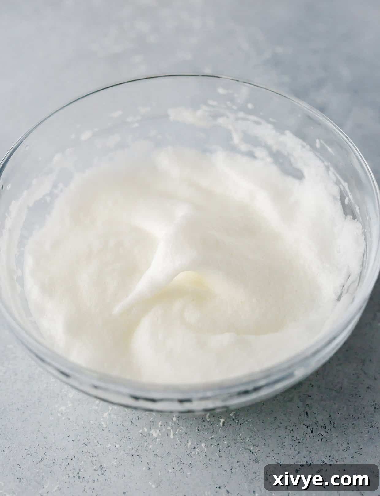 A close-up shot of perfectly whipped egg whites, forming soft, glossy peaks in a clear glass bowl, ready to be incorporated into the pancake batter.