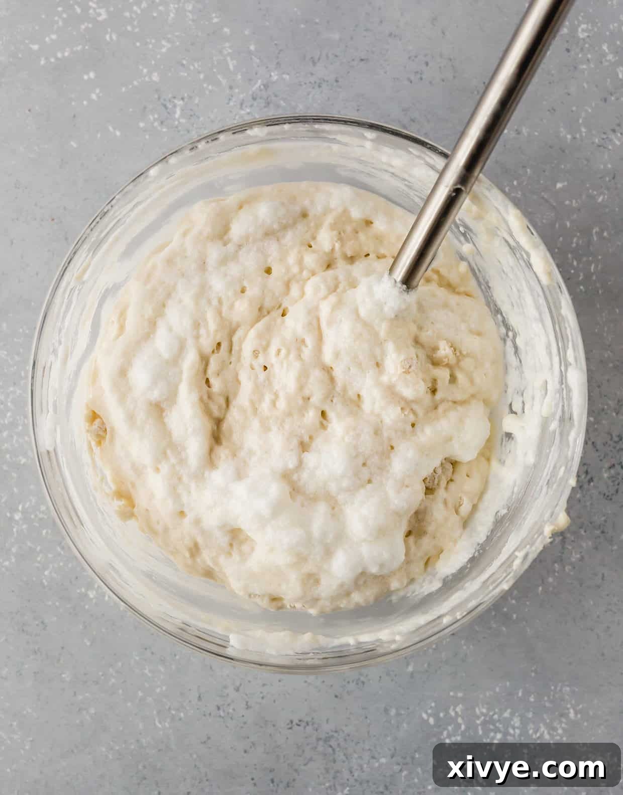 A glass bowl filled with fluffy buttermilk pancake batter, showcasing its ideal lumpy texture, set against a subtle gray background, ready for cooking.
