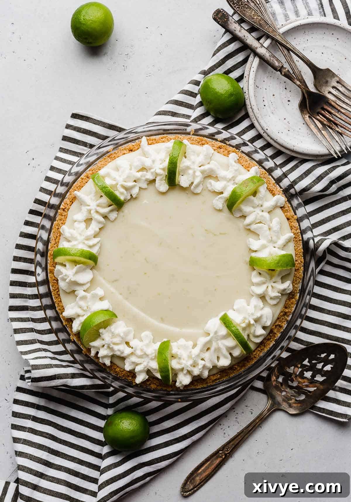 Velvet Key Lime Pie with a Sour Cream Kiss 5 Overhead photo of a key lime pie topped with a generous border of whipped cream and garnished with lime wedges.