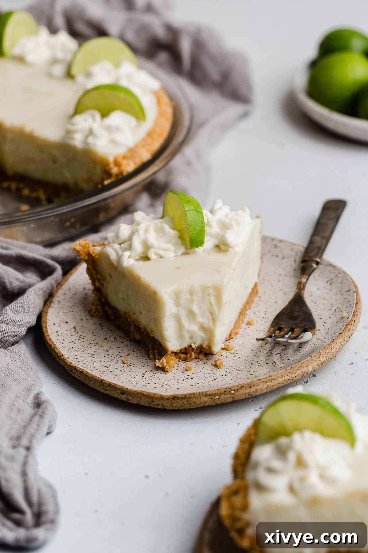 Velvet Key Lime Pie with a Sour Cream Kiss 7 A delectable slice of easy Key Lime Pie on a white plate, showcasing its golden crust, creamy filling, and fresh lime garnish.
