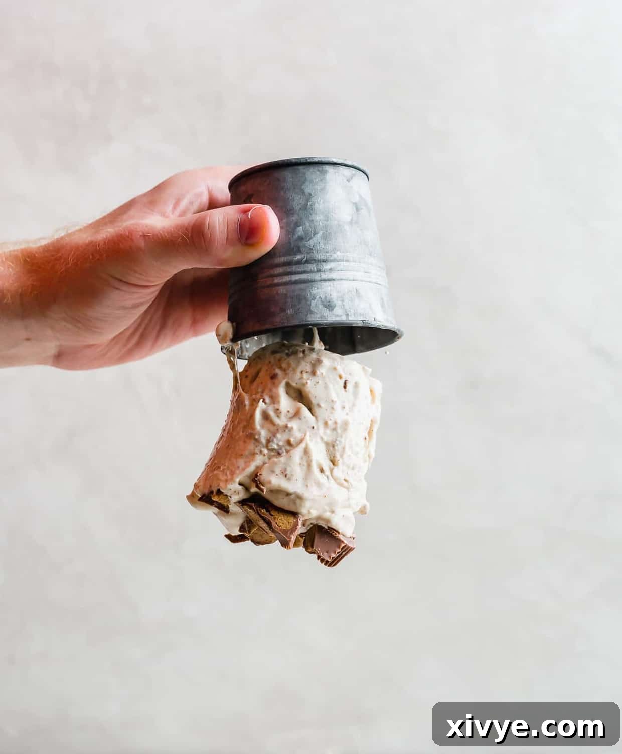 A hand holding a metal cup upside down with ice cream falling out of the cup!