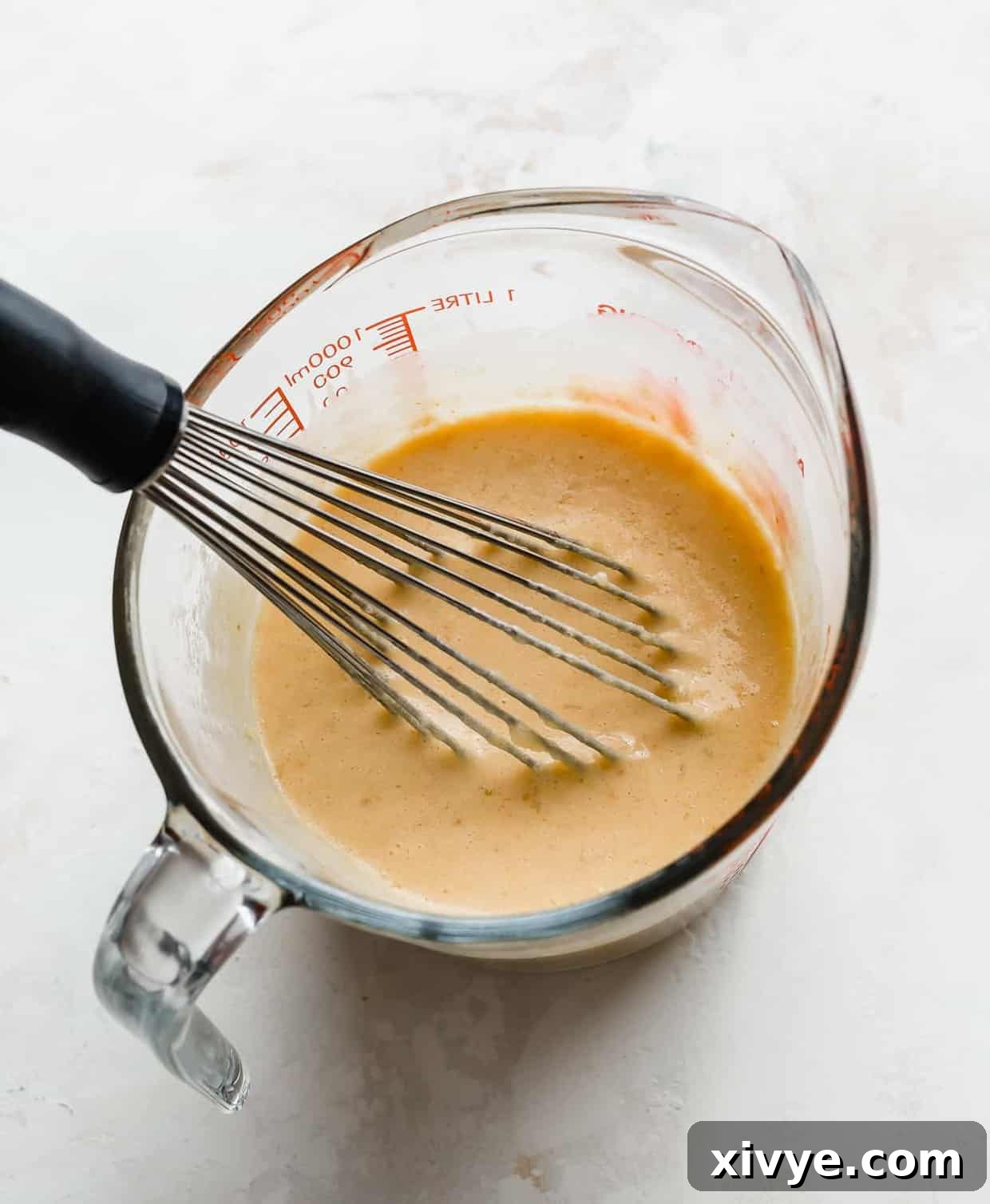 A clear glass measuring cup holds a vibrant mixture of pumpkin puree, creamy buttermilk, rich egg yolks, and melted butter, ready to be combined with dry ingredients.