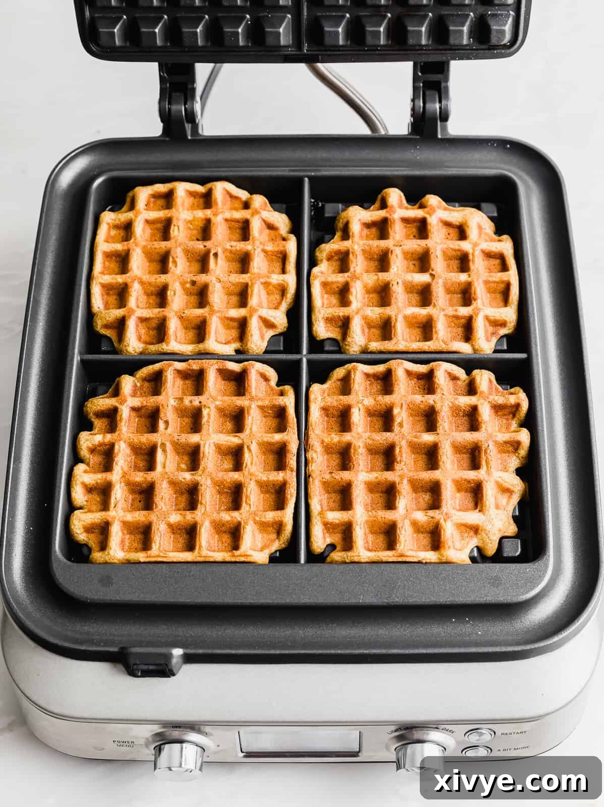 Four perfectly cooked square pumpkin waffles nestled within a waffle iron, showcasing their golden-brown, crispy edges and fluffy appearance.