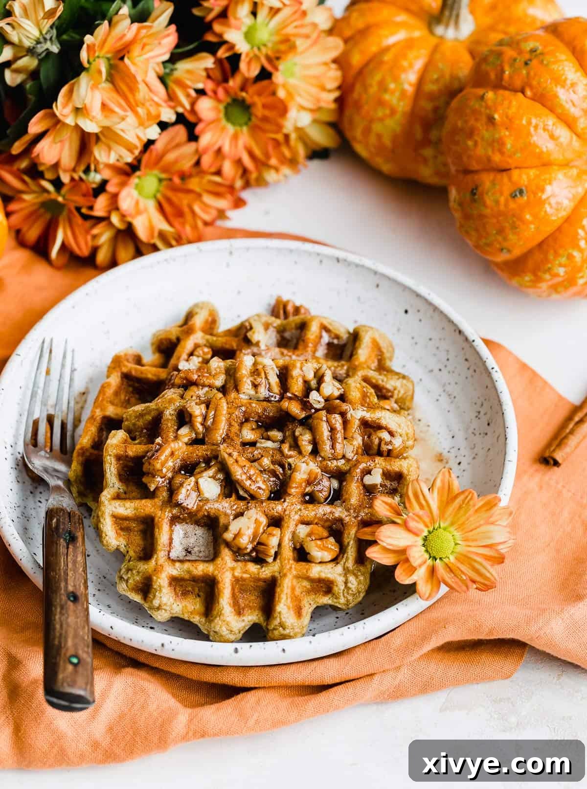 Two beautifully plated Buttermilk Pumpkin Waffles, generously topped with a sprinkle of pecans, on a pristine white dish, ready to be enjoyed.