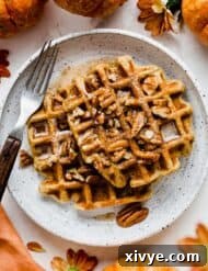 Two pumpkin waffles on a white plate, topped with pecans and syrup.