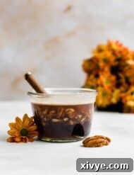 A glass jar full of Cinnamon Brown Butter Pecan Syrup, with orange flowers in the background.