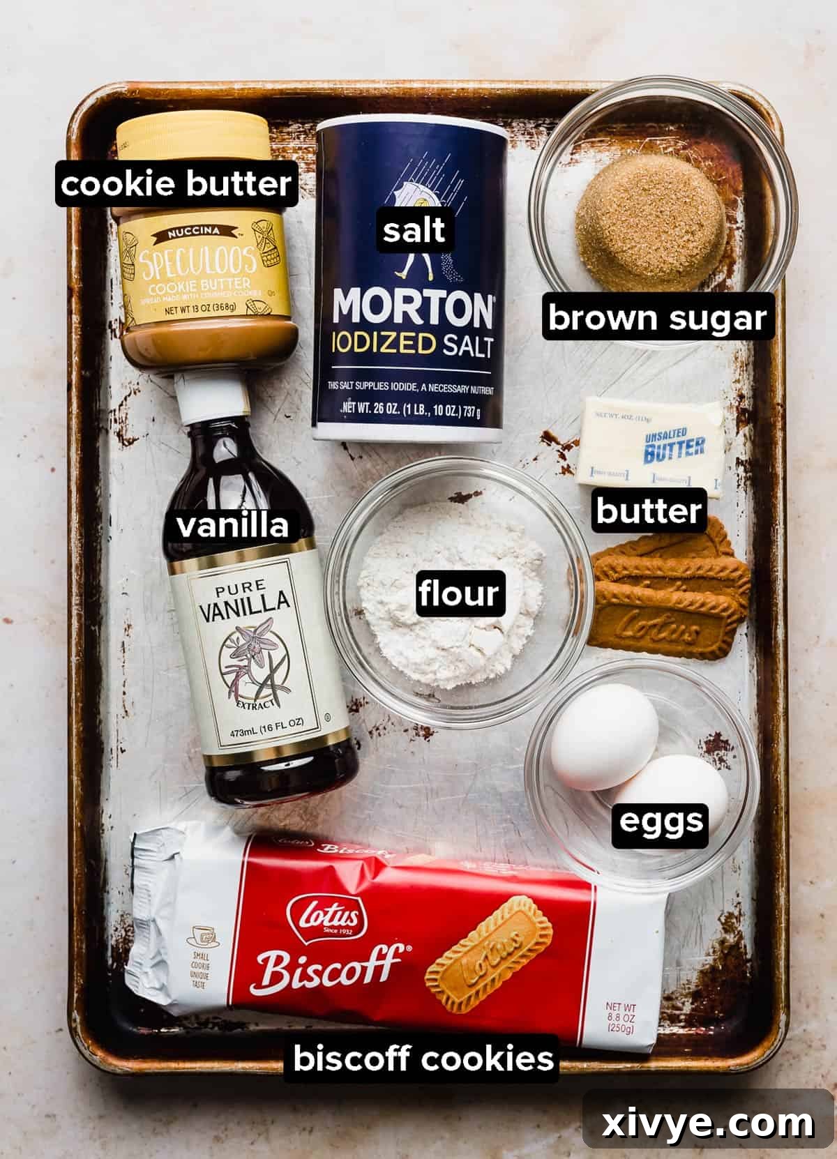 Biscoff Brownies ingredients placed on a worn baking sheet on a white background.