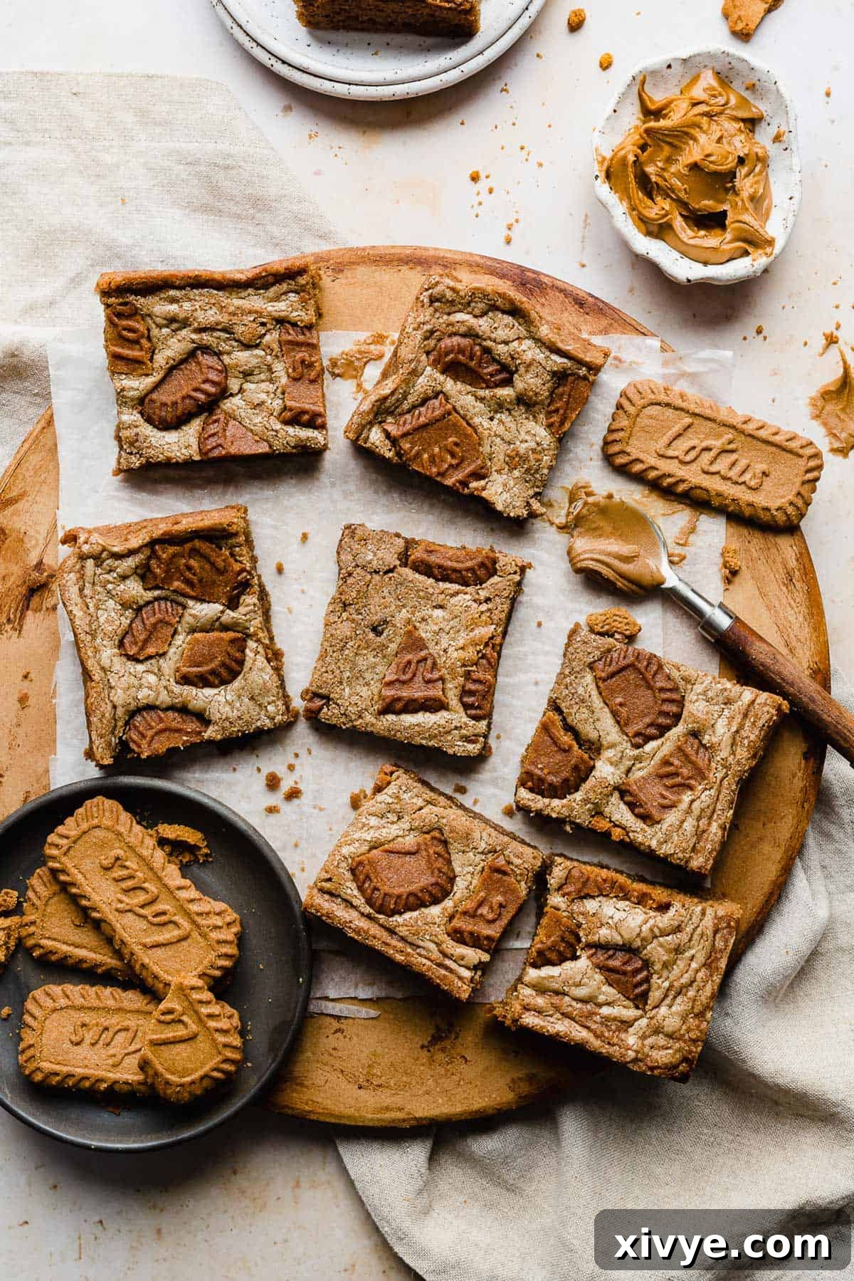 Biscoff Brownies cut into squares resting on a white parchment paper that's on a brown round board.