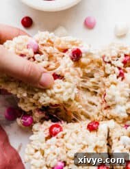 A hand pulling a square of M&M Rice Krispie treats, showcasing the texture.