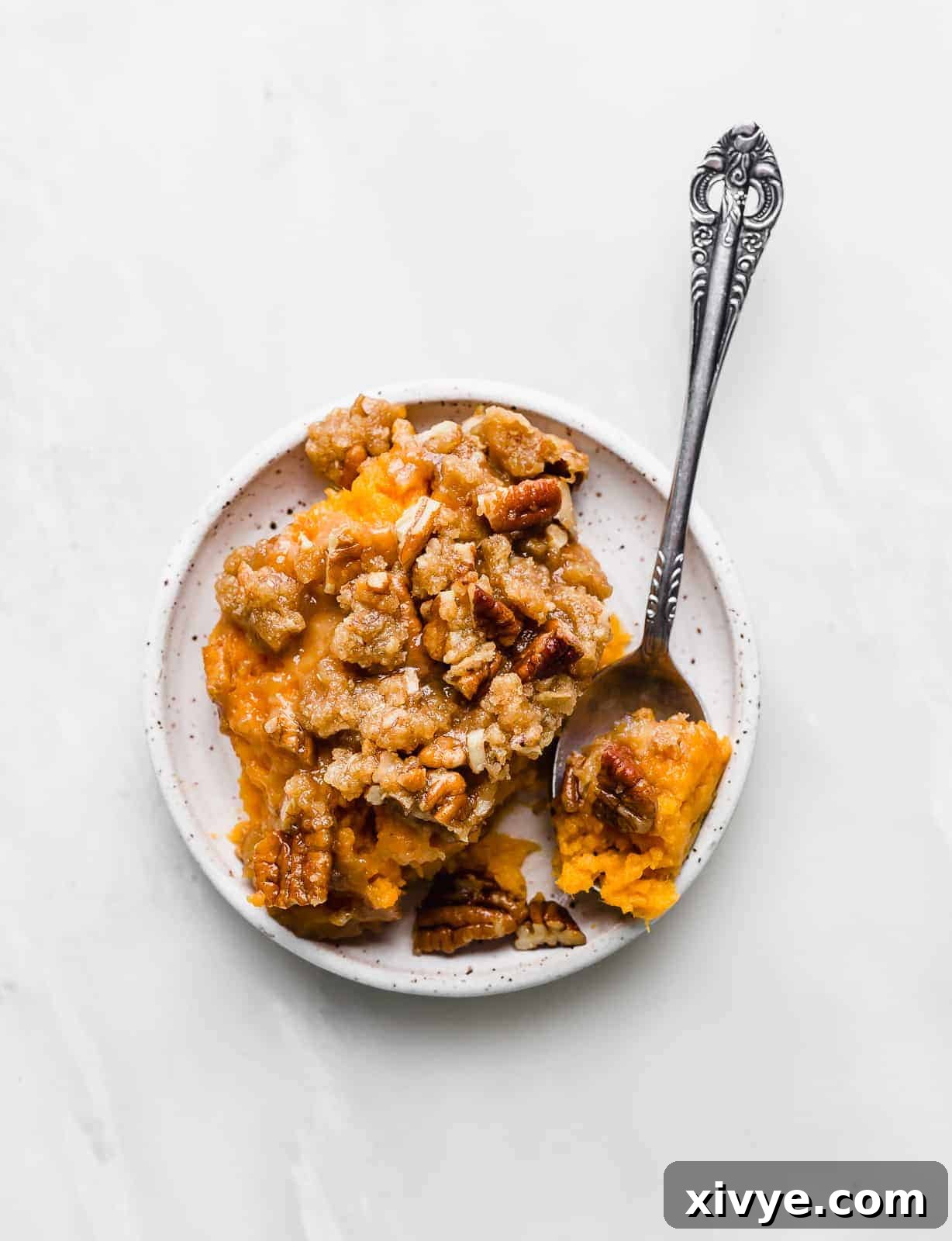 Effortless Sweet Potato Bake 2 A white plate with a generous serving of Sweet Potato Casserole topped with golden brown pecan crumble.