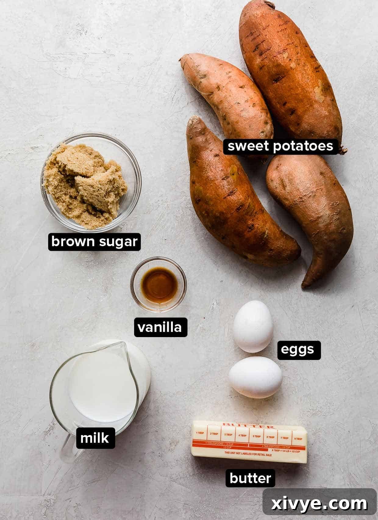 Effortless Sweet Potato Bake 3 Easy Sweet Potato Casserole main ingredients laid out on a light gray background: vibrant orange sweet potatoes, milk, butter, eggs, vanilla extract, and brown sugar.