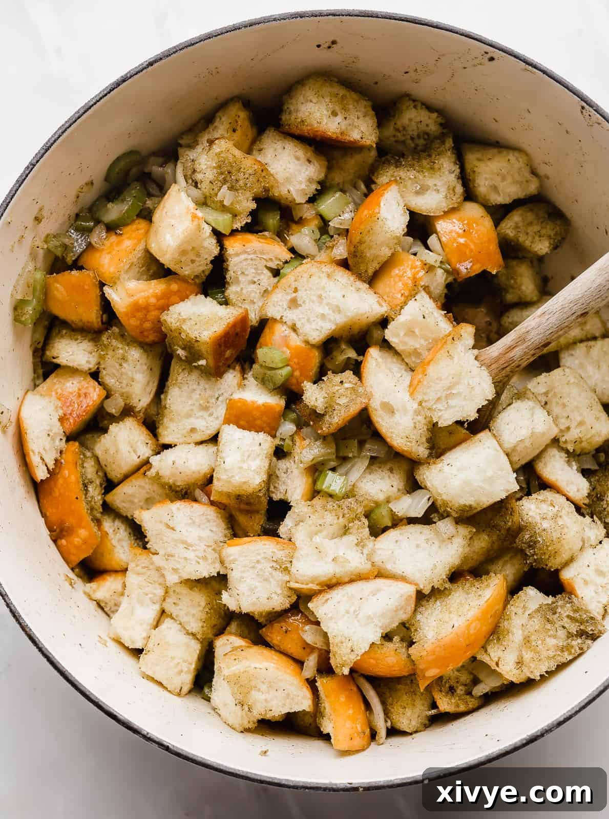 The Ultimate Thanksgiving Stuffing 5 Cubed bread in a large dutch oven with a wooden spoon sitting in the pot too.