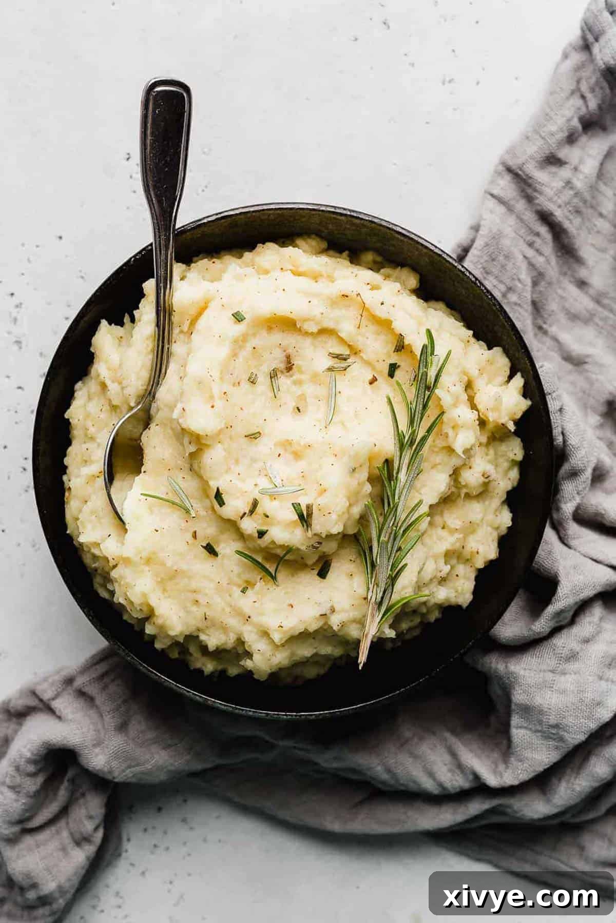 A black bowl filled with Rosemary Brown Butter Mashed Potatoes topped with a sprig of fresh rosemary, ready to be served.