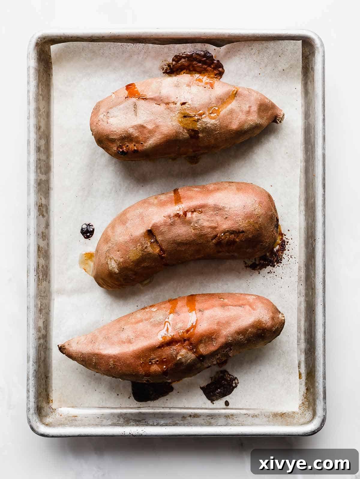 Golden Baked Sweetness 5 Three perfectly Baked Sweet Potatoes on a white parchment lined baking sheet.