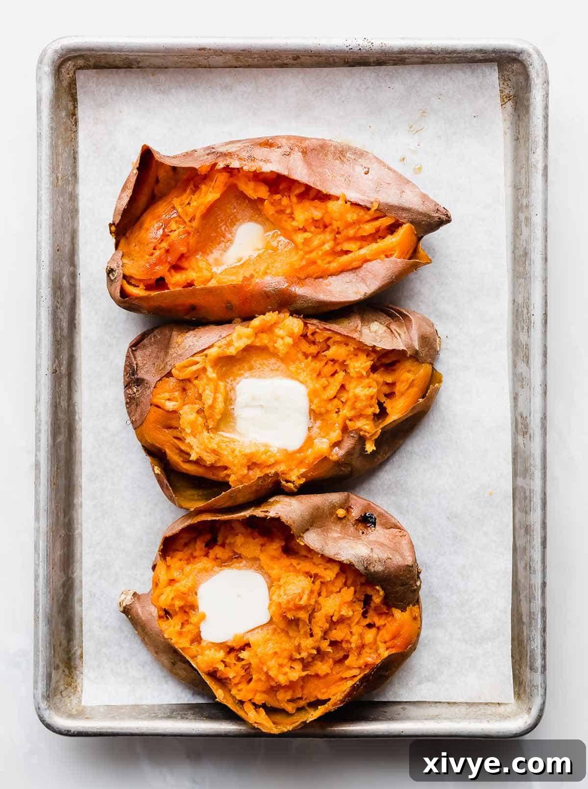 Golden Baked Sweetness 6 Three baked sweet potatoes on a baking sheet, each cut open with a square of butter in the orange flesh.