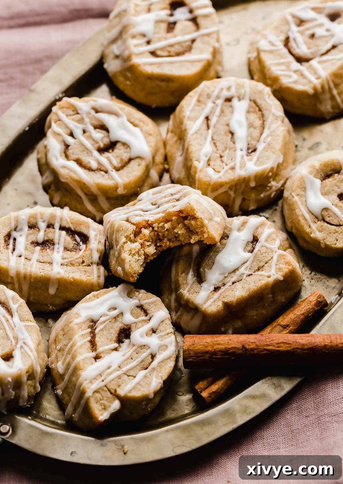 Glazed Cinnamon Roll Cookies on a bronze plate with one cookie having a bite taken out of it.