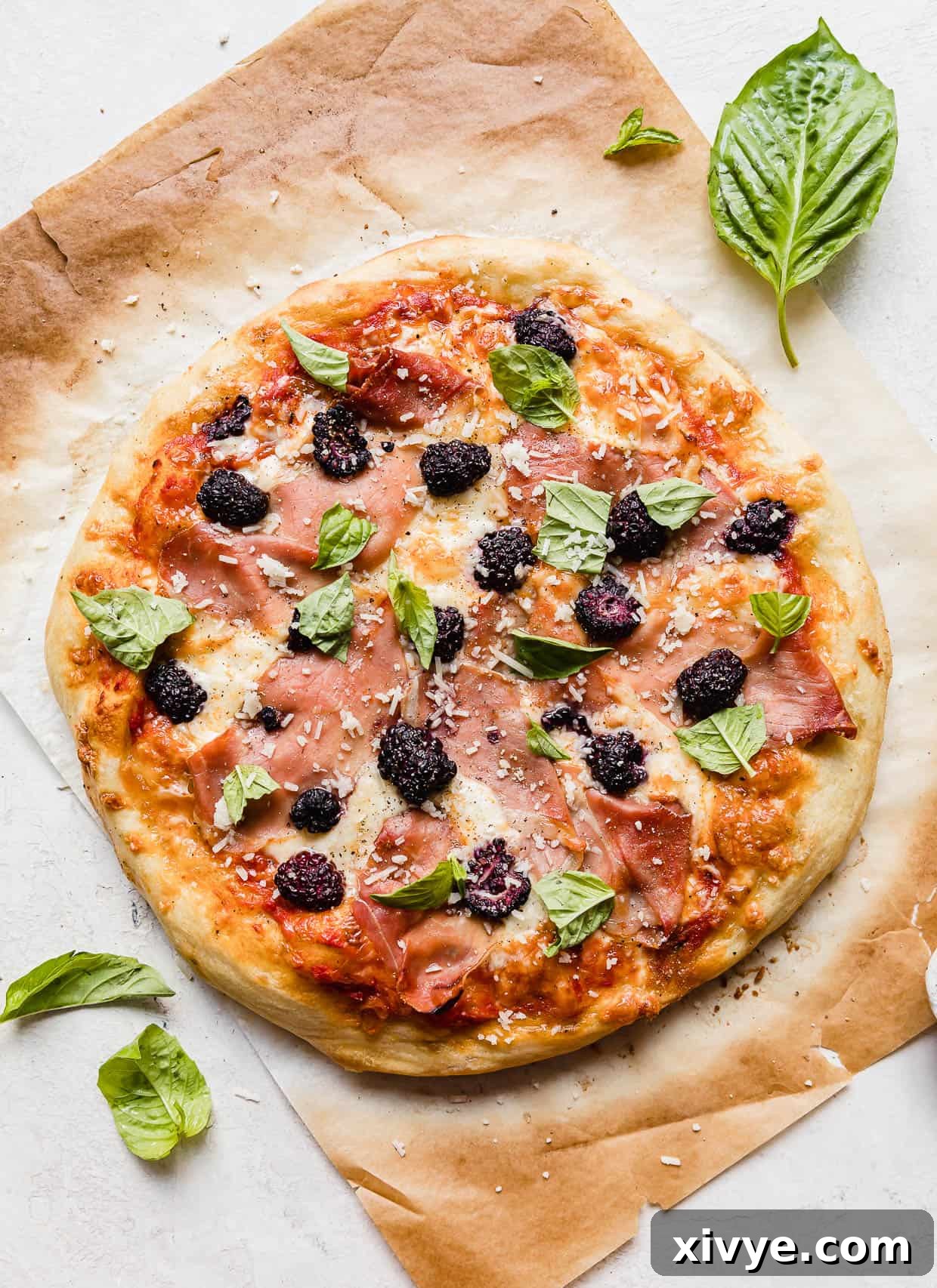 Blackberry pizza topped with fresh basil and parmesan on a brown parchment paper, ready to be sliced.