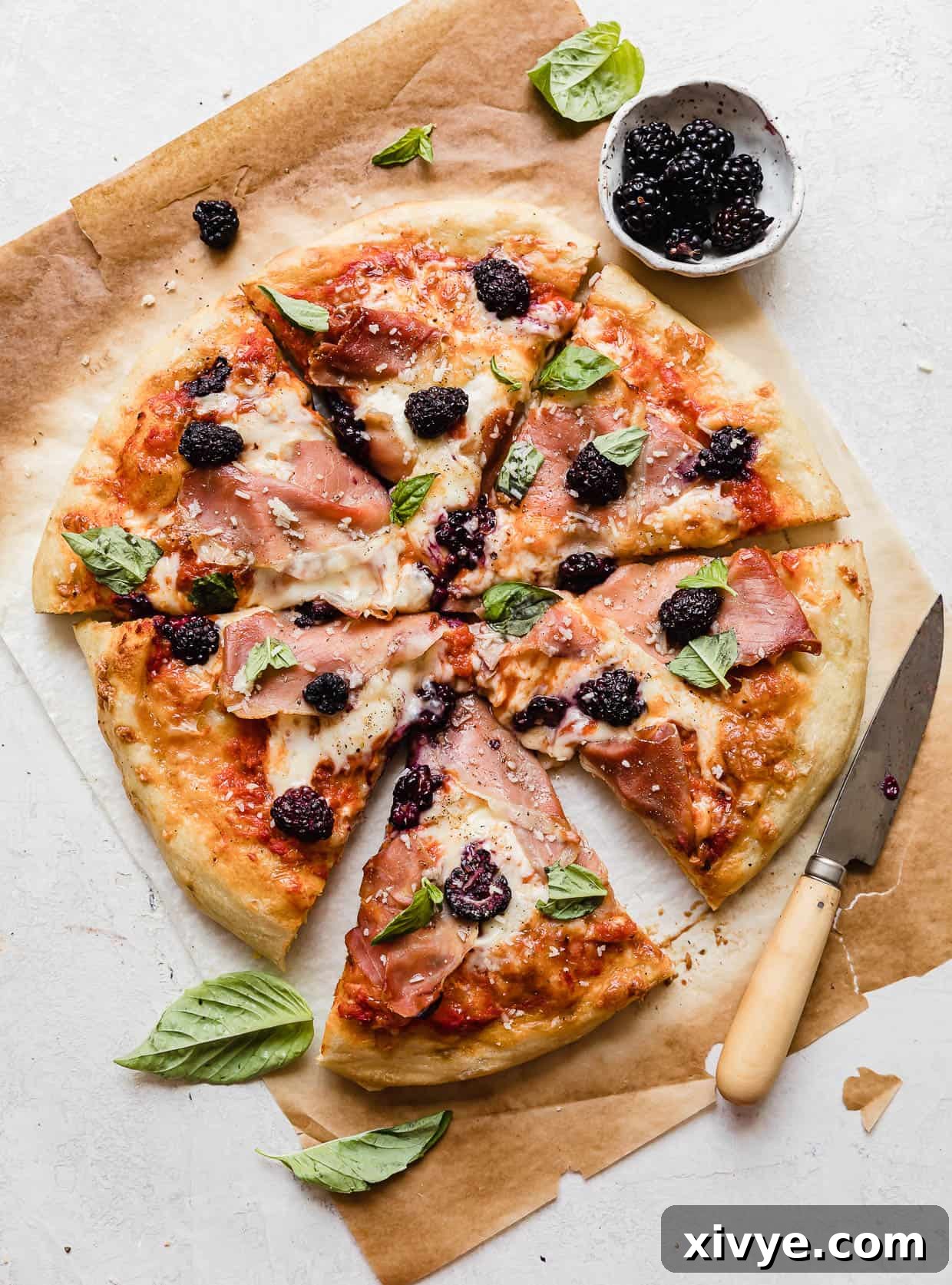 Blackberry Pizza topped with fresh basil and parmesan on a pristine white background, showcasing its artistic presentation.