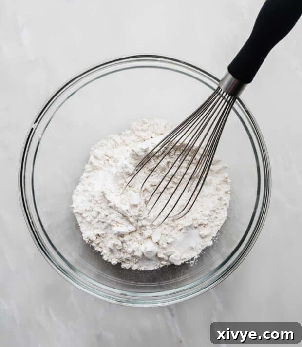 A glass bowl containing white flour and a metal whisk, ready for mixing the dry ingredients for banana bread.