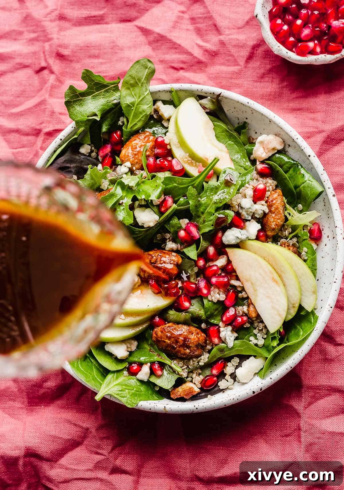 Freshly prepared Pomegranate Salad being generously drizzled with its homemade pomegranate dressing, highlighting the vibrant colors and tempting textures.