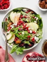 Pomegranate Salad topped with pears, pomegranate arils, pecans, and cheese, on a white background.