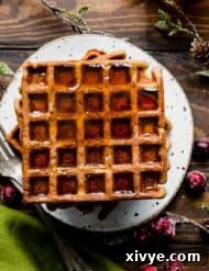 The best gingerbread waffles on a white plate covered in maple syrup.