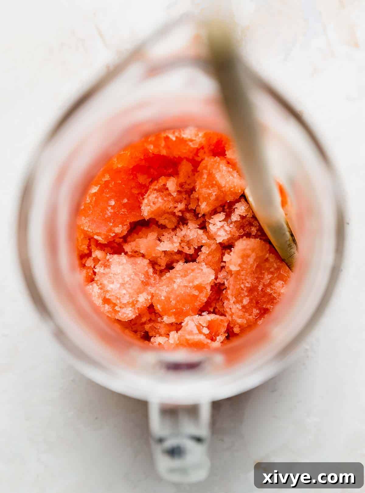 An overhead shot captures a vibrant red cranberry slush in a large, clear pitcher, showcasing its inviting frosty texture, ready to be served as a refreshing holiday beverage.