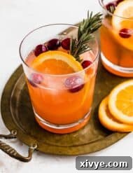 A clear glass filled with Christmas Slush Punch fresh cranberries and an orange slice.