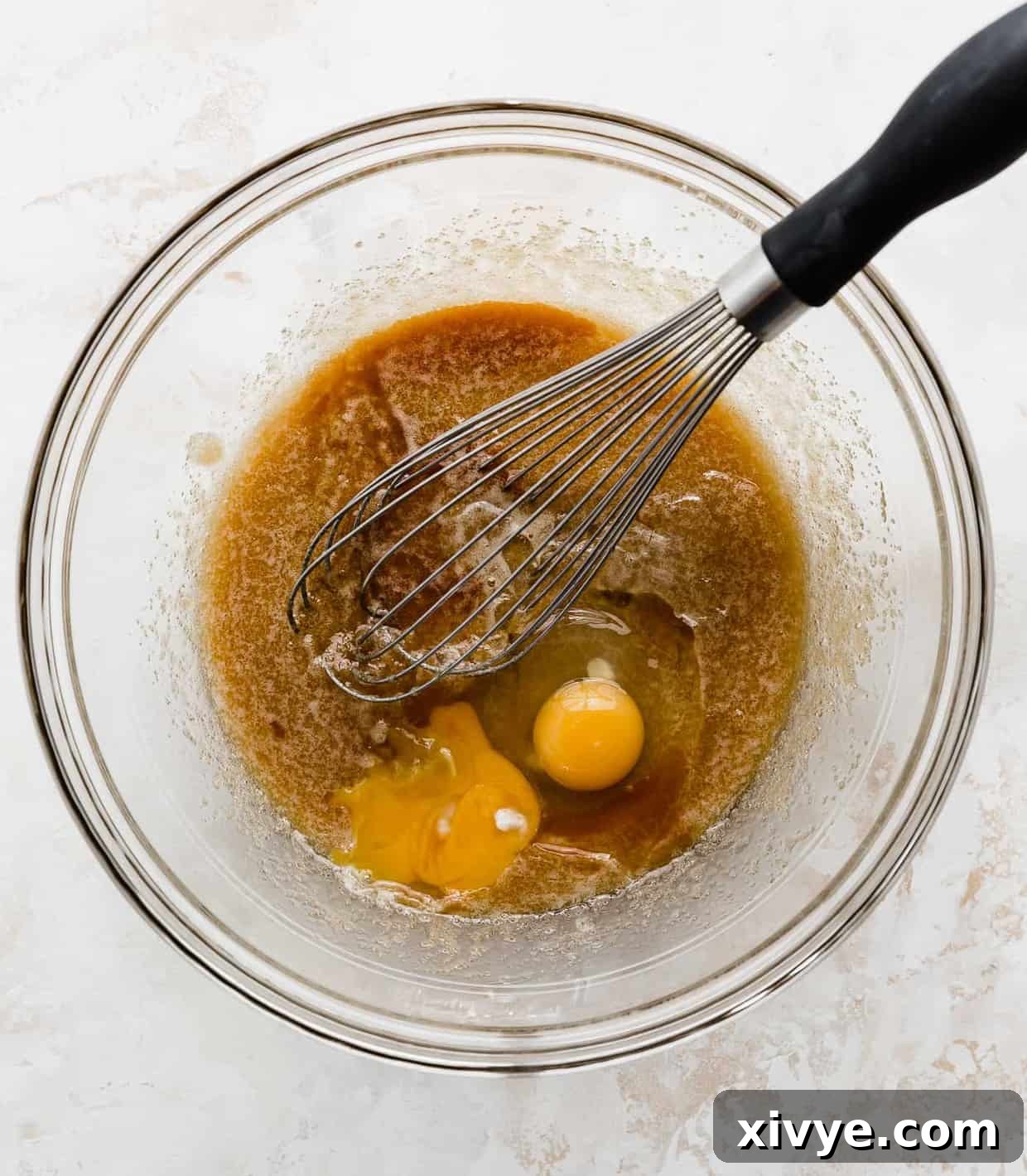 Brown sugar, melted butter, eggs, and vanilla in a glass bowl being mixed by a whisk.