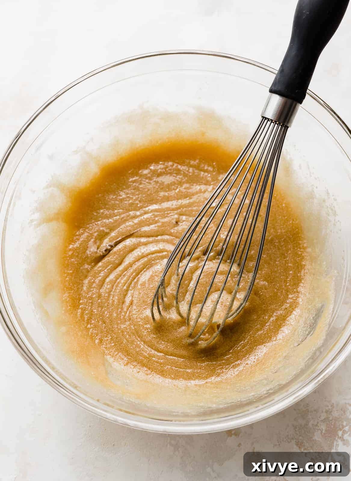 The wet ingredients for Chocolate Chip Cookie Bars begin mixed in a glass bowl.