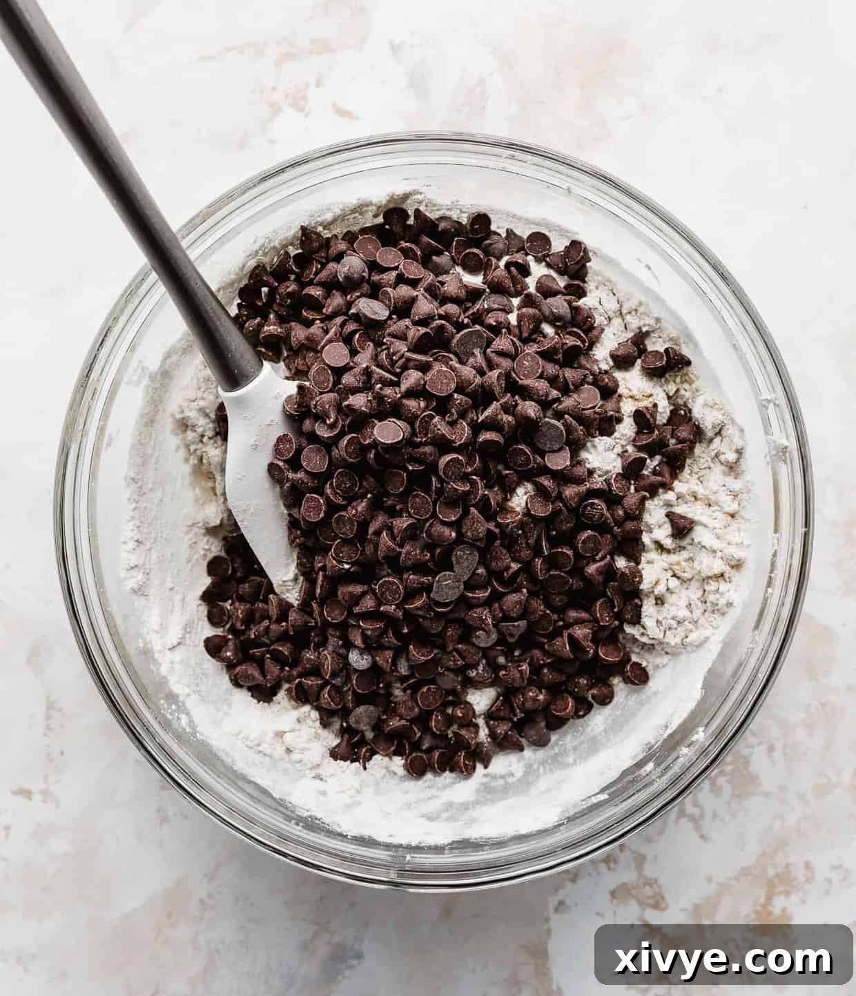 Chocolate chips overtop a mixture of dry ingredients in a glass bowl.