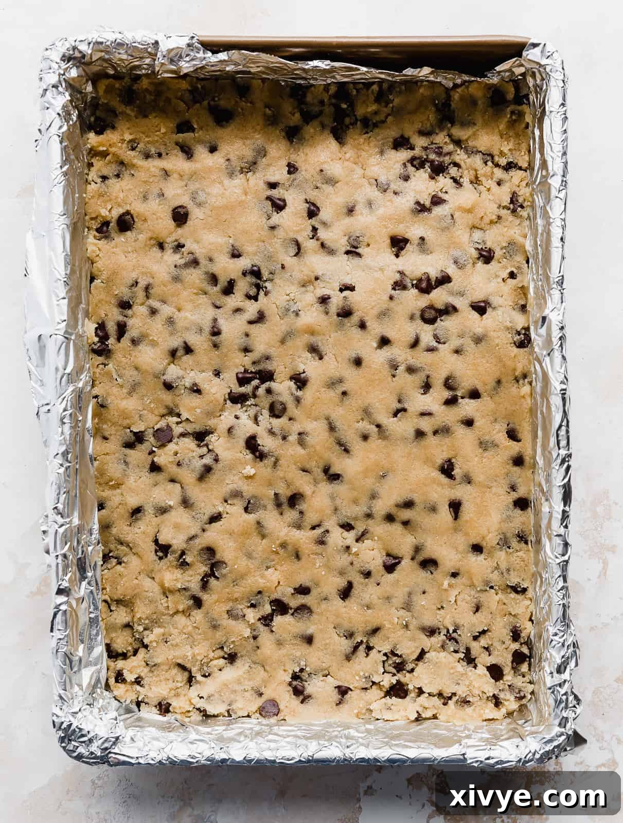 A 9x13 inch baking dish with chocolate chip cookie dough pressed into the pan.